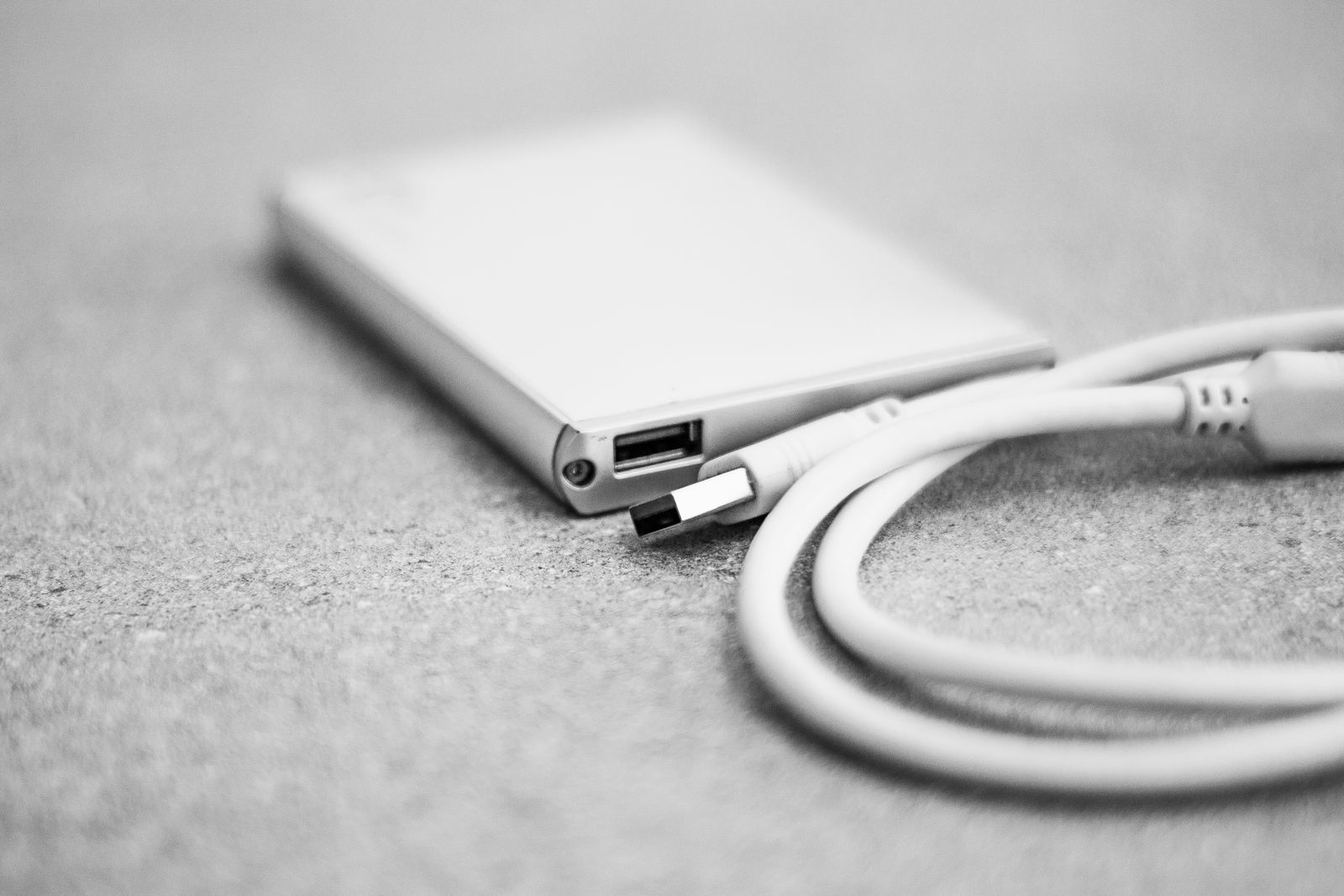 A small external USB drive with its cable on a desk, the kind of drive your photos are copied to, with nothing sent to the cloud